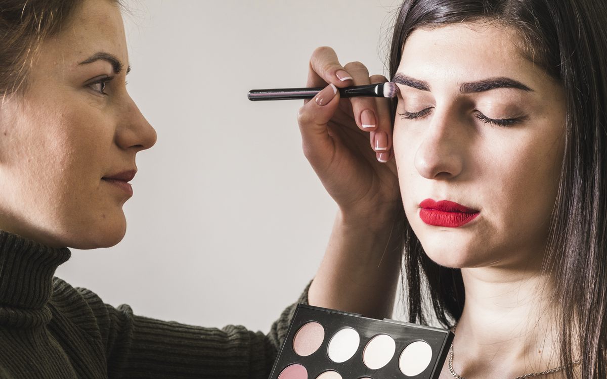 Makeup artist applying eyeliner, holding an eyeshadow palette